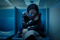 ID-2. Woman sitting huddled alone in a police precinct booth.