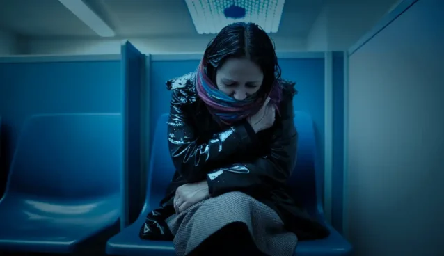ID-2. Woman sitting huddled alone in a police precinct booth.